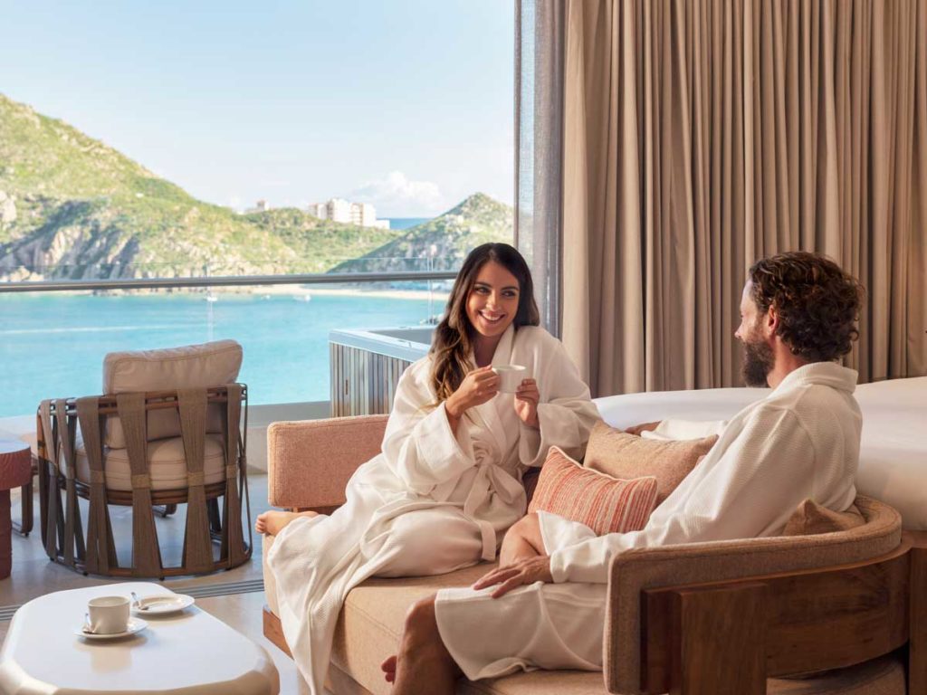 Couple Wearing Robes And Drinking Coffee In Their Guestroom.
