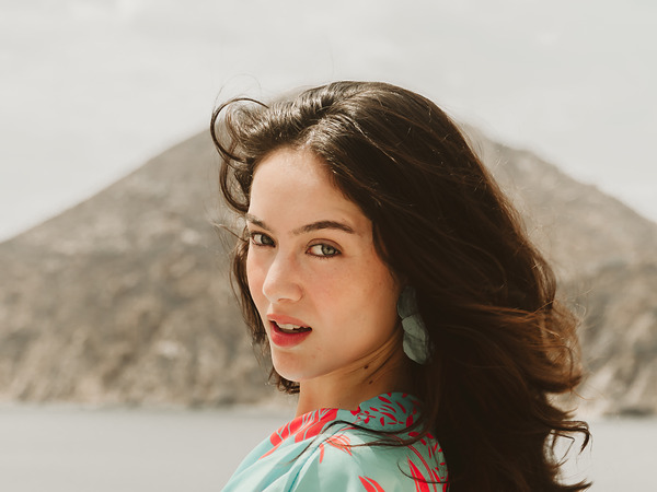 Woman with windswept hair in a coral and turquoise print smiling aboard a yacht near Cabo San Lucas, home of Corazon Cabo Resort & Spa