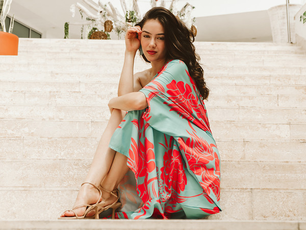 Woman in a coral and turquoise floral maxi dress seated on travertine steps at a modern resort in Cabo San Lucas